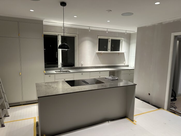 Nyligen renoverat kök med moderna skåp, bänkskiva och enkel pendellampa, väggar redo för målning.