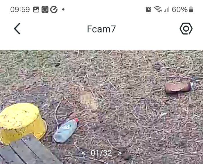Övervakningskamerabild visar utomhusmiljö med leksaker och skor på marken under dagtid.