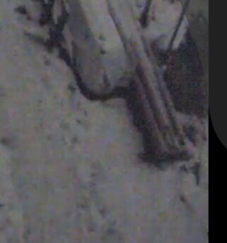 Övervakningskamera bild på snötäckt mark med grenar, inzoomad för att demonstrera bildkvalitet nattetid utan IR.