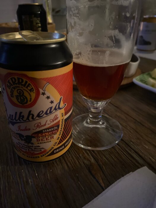 En burk India Red Ale bredvid ett halvtoms glas med öl, på ett mörkt träbord.