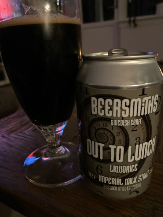 Ölglas fyllt med stout bredvid en burk Beersmiths "Out to Lunch" Imperial Milk Stout på ett bord.