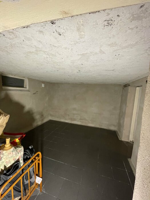 Ett källarrum med flagnande och ojämnt innertak samt putsade väggar och mörkt klinkergolv.