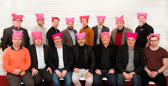 Grupp människor som bär rosa mössor, står och sitter i två rader.