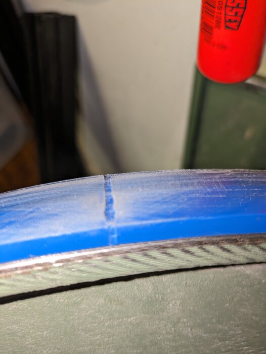 Svetsfog på ett blått polyuretanband nära kanten, där bandet möter grå maskindel.