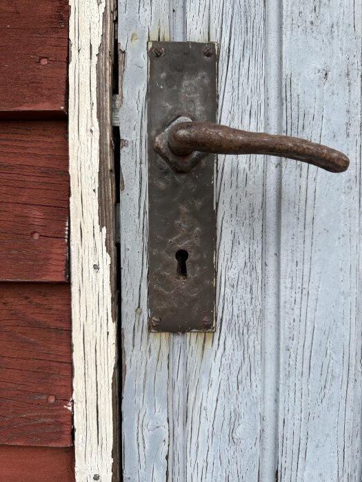 Gammal rostig dörrhandtag med låsplatta på ett vitmålat uthus.