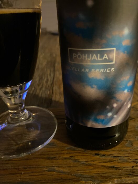 Ölglas och flaska av Põhjala Cellar Series på ett träbord, implyerar lagring på whiskyfat.