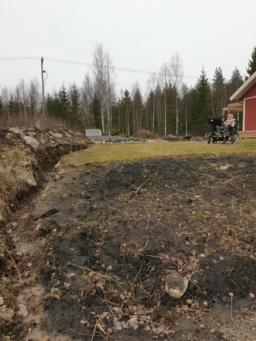 Uppgrävd gräsmatta med synliga vattenansamlingar och en barnvagn i bakgrunden.