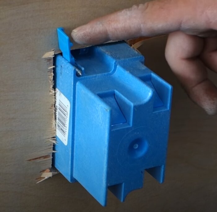 Blå apparatdosa för gipsvägg monterad i öppnad gipsskiva, hand pekar på dosan.