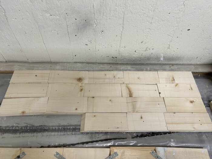 Träplankor upplagda på golvet, varav några med hålband och andra limmade, i en byggprocess.