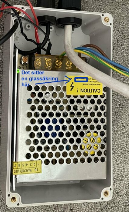 Elektronikenhet med öppet lock som visar kretskort med inbyggd glassäkring och anslutna kablar.