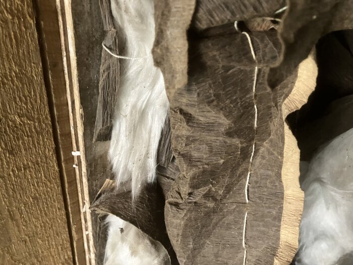 Närbild på äldre isoleringsmaterial som kan vara glasull eller asbest, monterad mellan träreglar.