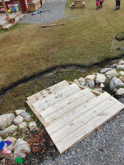 Nygrävt dike runt en köksträdgård, omgivet av gräs och sten, med en träpall framför.