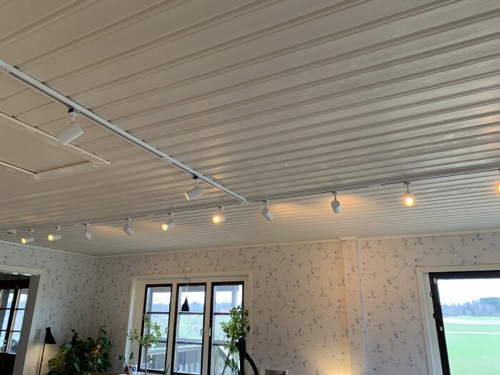 Belysningsskena med lampor monterad i vitmålat tak, trådlös styrning i inomhusmiljö.