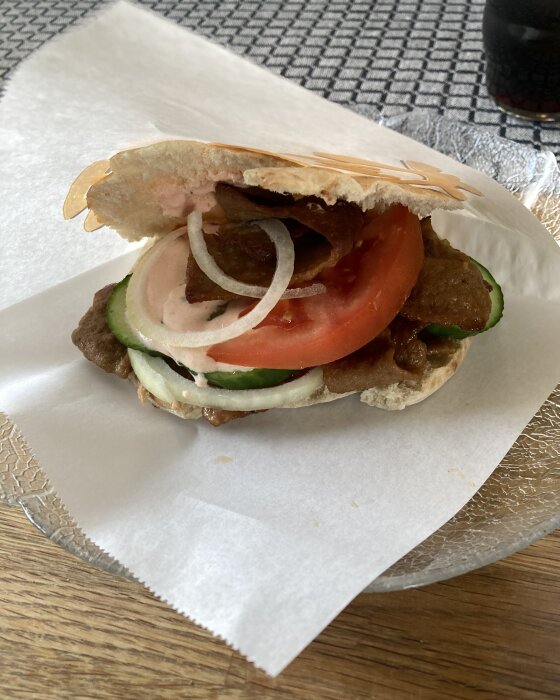 Kebabrulle med sallad, tomat, lök och sås på en vit pappersduk.