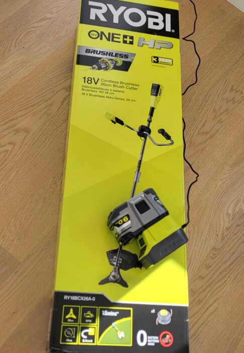 RYOBI 18V sladdlös grästrimmer i originalförpackning på ett träbord.