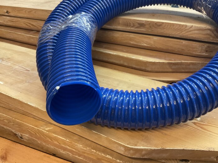 Blå PVC-slang med slät insida som är tänkt för anslutning till dammsugaren i en verkstad.