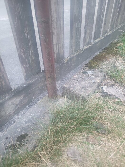 Glipa mellan gammalt trästaket och skadad betongsockel på sluttande mark.