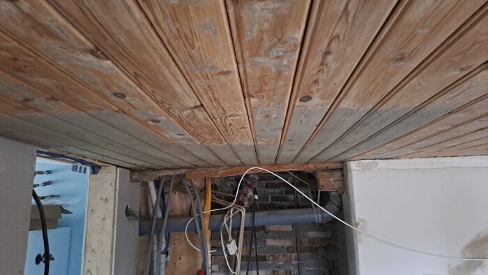 Renoverat vardagsrumstak med synliga träbjälkar och skrapade takbrädor, exponerad isolering och kablar.