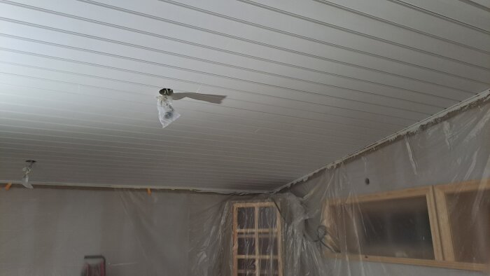 Nymålat vitt tak i vardagsrum med skyddsplast och synliga elledningar.