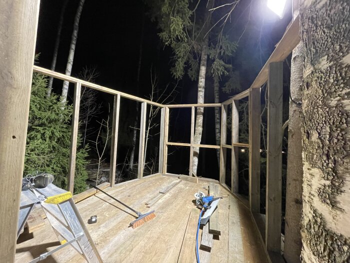 En trädkoja under konstruktion om natten med väggreglar, verktyg och träd runtomkring.