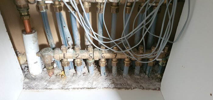 Oorganiserade golvvärmerör och fördelarventiler utan fördelarskåp synliga i ett utrymme.