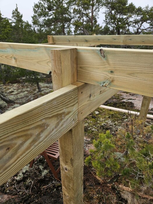 Träkonstruktion med stolpar och bärreglar vid ett byggprojekt i ett skogsmiljö, visar detalj av sammanfogning och skruvförband.