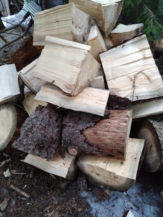 Hög med nysågade trädstammar och vedklabbar i olika storlekar på marken.