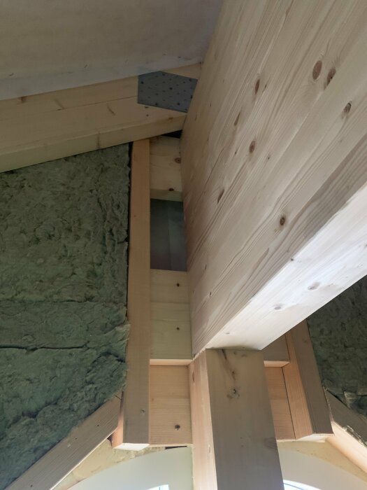 Trångt utrymme med träbjälkar och monterad stenullsisolering i byggkonstruktion.