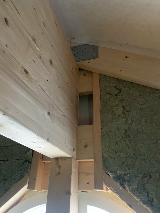 Trångt utrymme mellan träbjälkar med delvis installerad isolering i en vindskonstruktion.