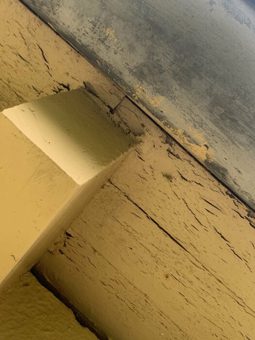 Närbild på en husfasad med sprucken och flagande gul färg vid en hörna där lacken lösts upp.