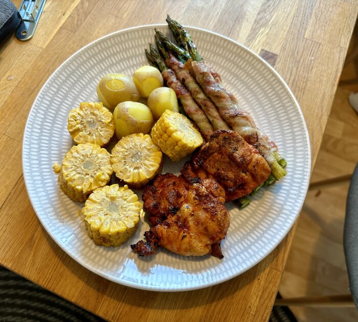 Grillade kycklinglår med potatis, majs och sparris på en tallrik.