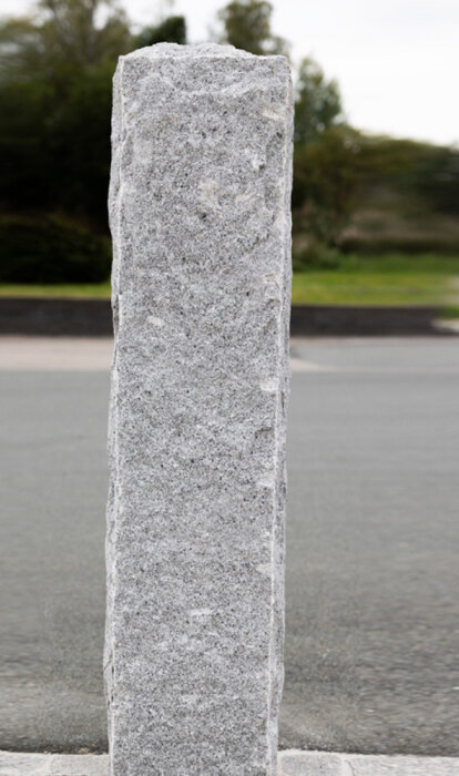 En stående granitstolpe på trottoarkant, väger ca 250 kg, använd för byggdiskussion.