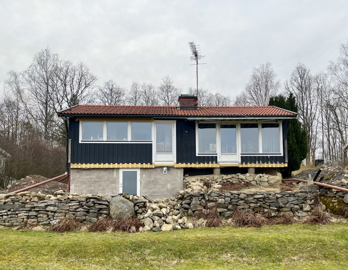 Ett enfamiljshus med tegeltak och stenkista på höjd framför grå himmel.
