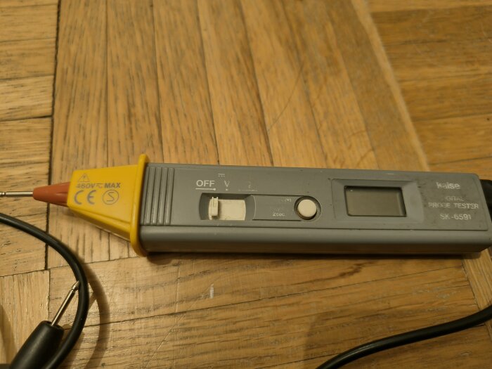 En använd multimeter av modell "Kaise SK-6591" med testsladdar på ett träbord.