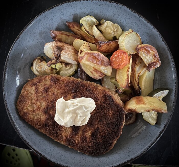 Panerad schnitzel med ugnsbakade grönsaker och klick bearnaisesås på grå tallrik.