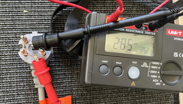 Isolationsresistansmätning på en spis med en multimeter och testledningar som visar 28,5 MΩ.