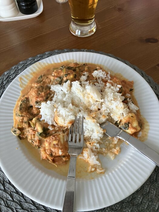 Tallrik med Palak Paneer och ris, modifierad med grillost och sivripaprika, bredvid glas med öl.