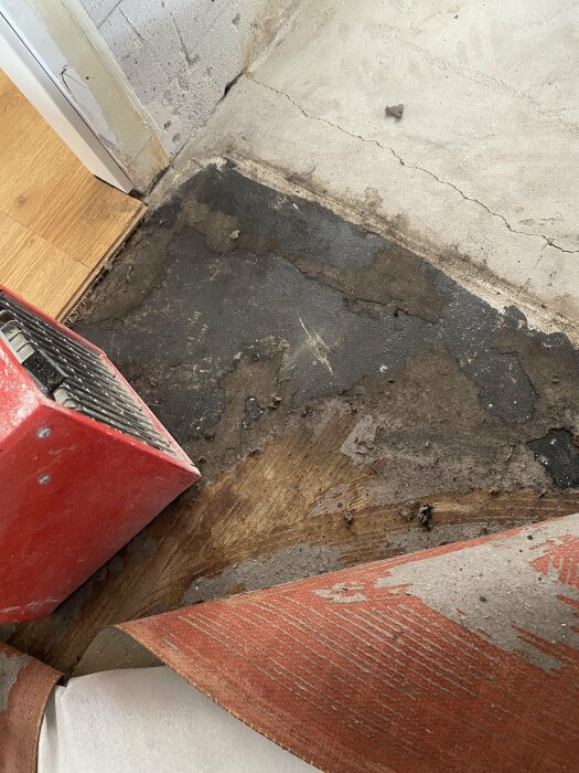 Mögelskador och rester av filmmaterial på betonggolv med synliga vattenskador nära avloppsrör.