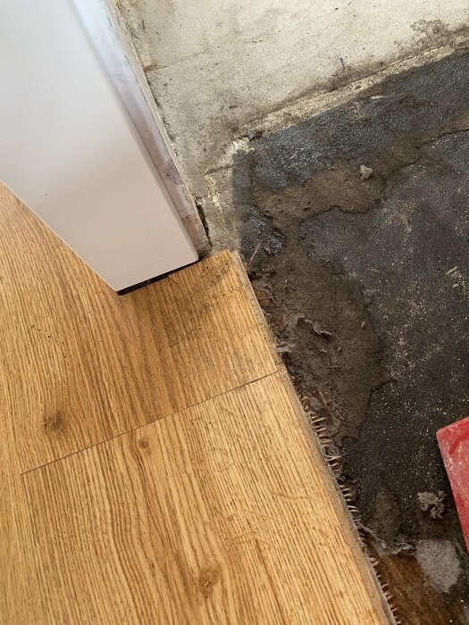 Närbild på skadat golv under diskmaskin med möjlig mögelskada och rester av en gammal plastmatta.