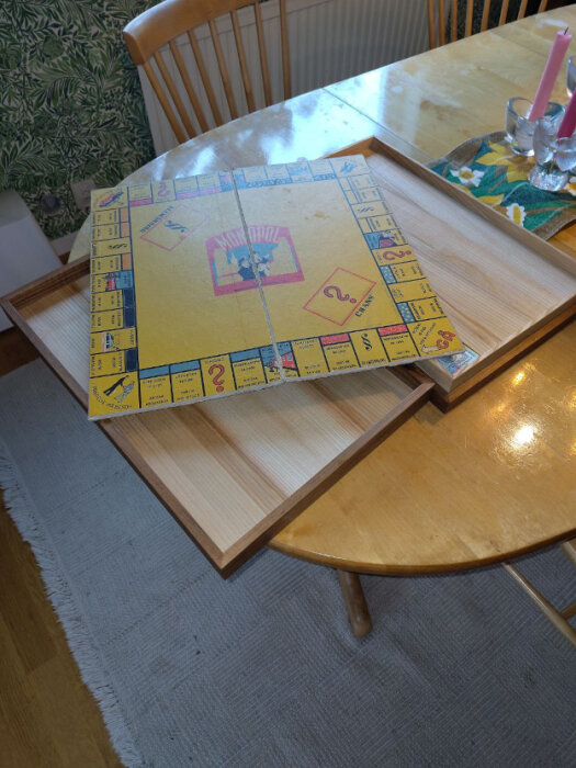 Gulbrun ask som rymmer ett uppfällt Monopol-brädspel på ett träbord.