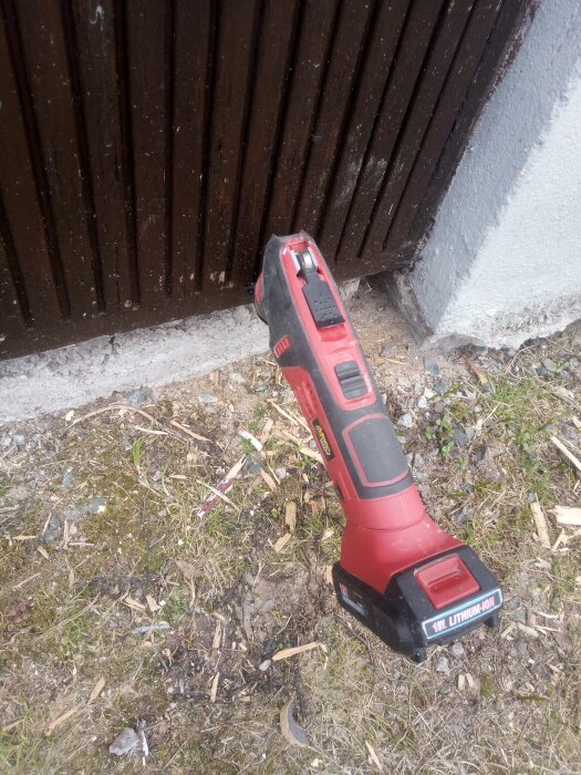 Röd batteridriven slipmaskin på marken bredvid en källardörr för att åtgärda en kärvar dörr.