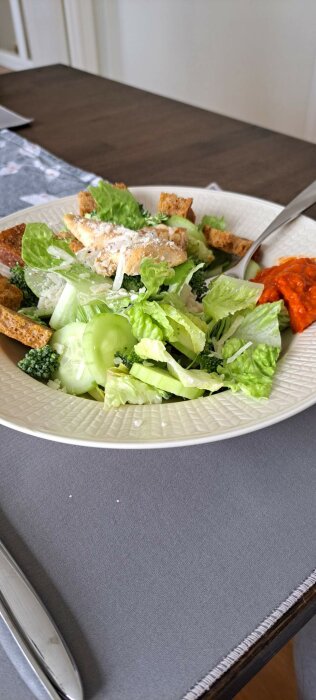 Caesarsallad med kyckling, krutonger, hyvlad parmesan och en klick ajvar på tallriken.