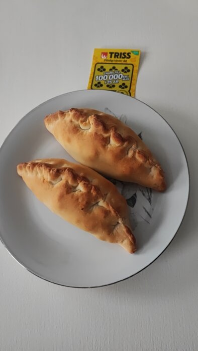 Två gyllenbruna mini calzone-pizzor på en tallrik med en Trisslott i bakgrunden.