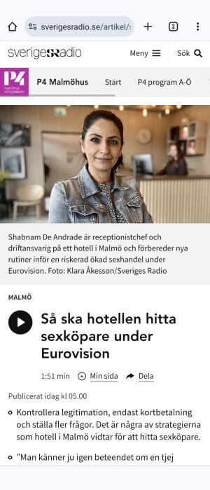 Kvinna i jeansjacka står i hotellreception med en person i bakgrunden som jobbar vid en dator.