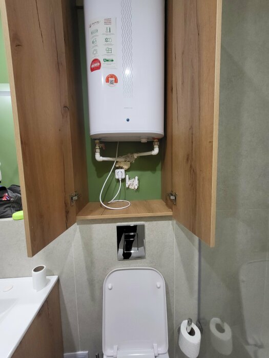 Vattenberedare ovanför toalett med synliga, potentiellt strömförande ledningar i ett hotellbadrum.