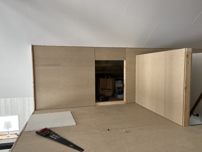Inredningsfas av ett loft med MDF-skivor som delvis täcker vägg och golv, synliga verktyg.