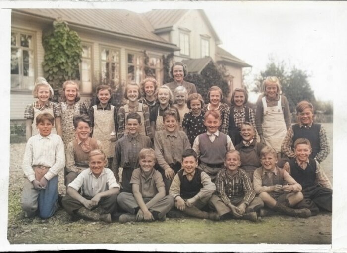 Färglagd historisk bild på en grupp leende barn framför ett hus blandat i könsfördelning och åldrar.