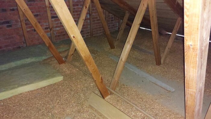 Träkonstruktion av takstolar i ett bygge med isolering och spån på golvet.