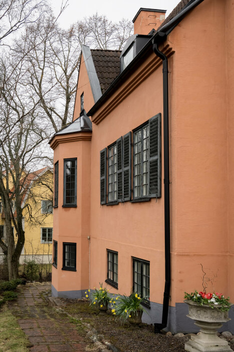 Hörn av en klassisk villa i Djursholm med orange putsad fasad, svarta fönsterluckor och en blommande trädgård.