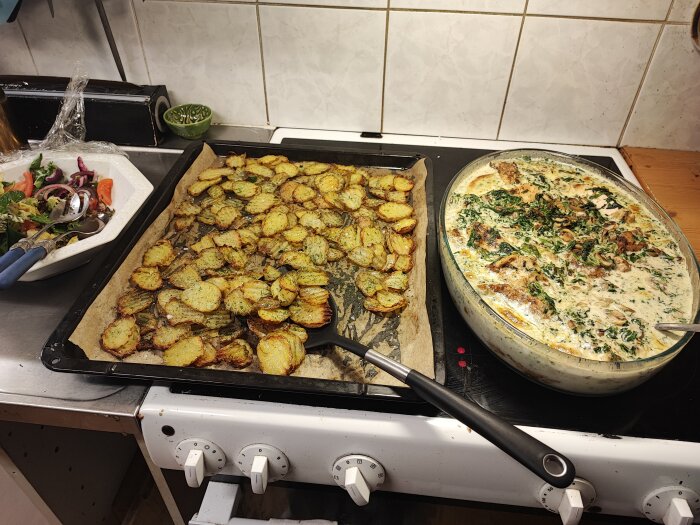 Hemgjorda reffel pommes på en plåt bredvid en gryta med creamy garlic chicken, samt sallad på köksbänken.